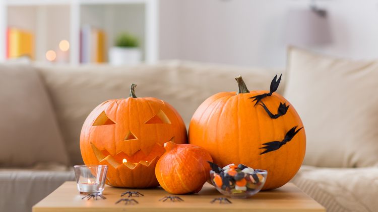 Three pumpkins, a candle, some black bats and a bowl of sweets on a table. The pumpkin has an eire 